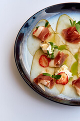 An Elegant Culinary Arrangement Featuring Thinly Sliced Pears, Prosciutto, Strawberries, and Creamy Cheese on a Stylish Plate Garnished with Fresh Herbs