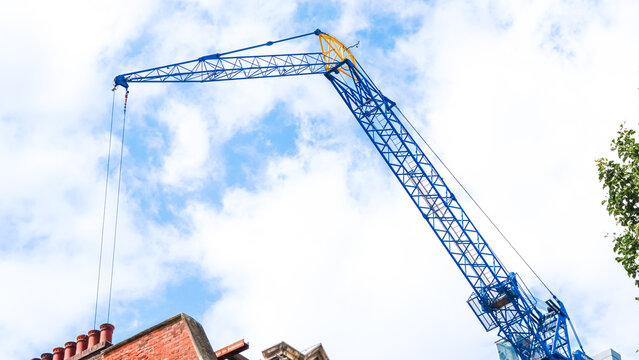 Tower crane lifting materials against clear blue sky at construction site - Powered by Adobe
