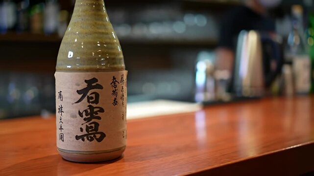 Ceramic sake bottle sits on a wooden bar, label with Japanese script