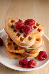 Stack of golden waffles with fresh raspberries