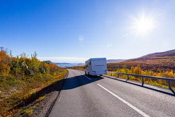 Motorhome driving on a scenic road in Kiruna, Sweden, with autumn foliage and beautiful lake views.