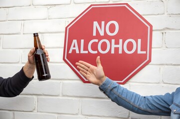 Person refusing alcohol with no alcohol sign on white brick wall in the background outside concept
