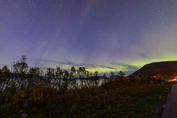 Northern lights in Kiruna, Sweden, reflecting on calm water in September with stars and forest in...