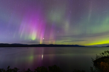 Northern lights in Kiruna, Sweden, reflecting on calm water in September with stars and forest in...