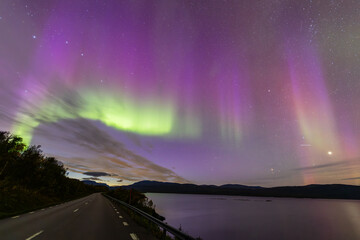Northern lights in Kiruna, Sweden, reflecting on calm water in September with stars and forest in...