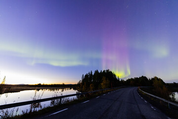 Northern lights in Kiruna, Sweden, reflecting on calm water in September with stars and forest in...