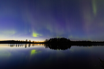 Northern lights in Kiruna, Sweden, reflecting on calm water in September with stars and forest in...