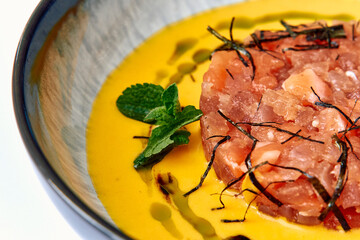 A tantalizing dish featuring a vibrant yellow sauce, tender meat tartare, garnished with fresh...