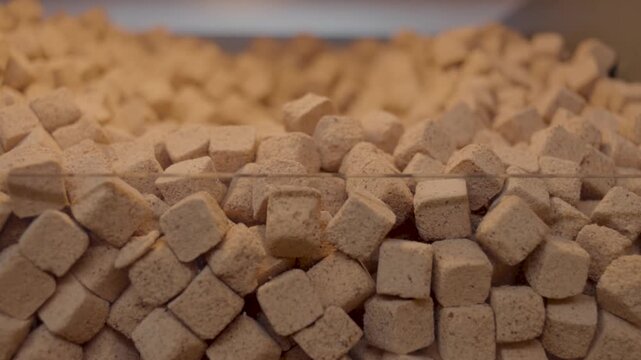 Close-up of beige-colored, cube-shaped dried food blocks neatly arranged in a wooden bin. These pieces resemble dried tofu or a similar product, and are displayed in bulk inside a natural-style