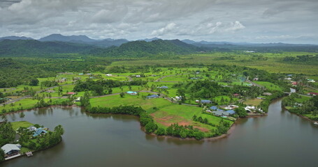 Drone capturing breathtaking scenery of Savusavu town featuring lush green landscape, meandering river, residential houses, and rolling hills in Fiji, showcasing tropical beauty and tranquility