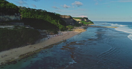 Aerial drone view of people relaxing, walking, swimming and surfing at Melasti Beach in Bali,...