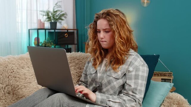 Young woman at home sitting with laptop feeling disappointed holding hand on forehead after failed attempt. Caucasian redhead girl on sofa frustrated, emotional reaction to unresolved online problem