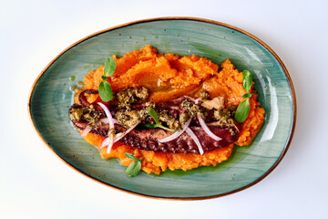 A beautifully plated gourmet dish of grilled octopus resting on a bed of silky sweet potato puree garnished with herbs and a tangy sauce, enticing the senses.