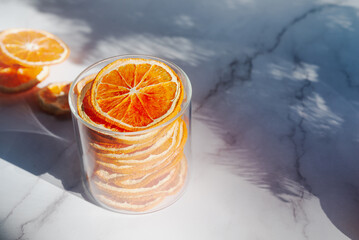 dried orange slices in a glass container on white marble table.