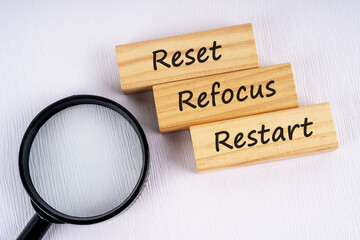 Magnifying glass and text reset, refocus and restart on wood block white background