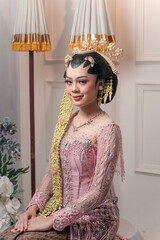 A beautiful Asian bride in a traditional pink Javanese kebaya with intricate beading and elegant...