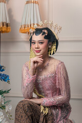 Elegant Asian bride in a pink Javanese kebaya with intricate beading, graceful jasmine accessories,...