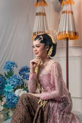 Side profile of an elegant Asian bride in pink Javanese kebaya, smiling softly with graceful...