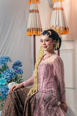 Elegant Asian bride wearing a pink beaded kebaya and traditional Javanese accessories, confidently...