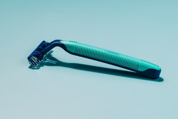 Blue and green manual razor diagonally on light blue. Symbolizes shaving, personal grooming, hygiene, and daily self care routines.