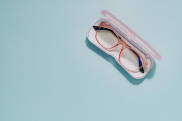 Pink framed eyeglasses in an open, translucent pink case on soft blue. Symbolizes eye care, protection, vision aids, and preserving delicate personal items.