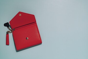 Stylish red wallet, partially open with tassel and heart keychain, on clean blue. Symbolizes personal finance, fashion, accessories, and giving receiving.