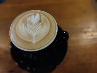 A cup of latte coffee with latte art decoration in the form of a rosetta leaf, served on a wooden...