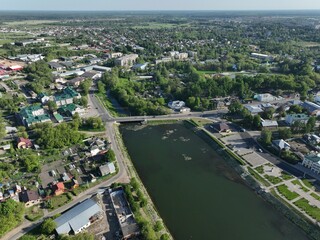 An aerial view of Kirzhach city, showcasing a river, a bridge, residential buildings, and lush green areas under a clear sky