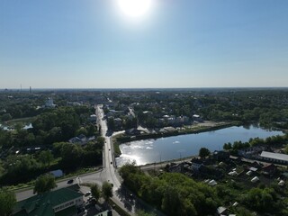 A wide aerial panorama of Kirzhach city, highlighting a large lake with sun reflection, a main road, and surrounding urban and natural landscapes