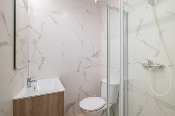 Modern bathroom with a shower, sink, and toilet. The walls are covered in light marble tiles. The space is clean and minimalistic, ideal for contemporary design.