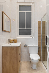 Modern bathroom with a shower, toilet, and wooden vanity. Bright tiles and a window provide natural light. Clean and minimalist design.