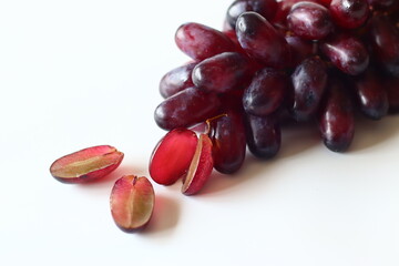 Fresh black seedless grapes, oval and elongated variety, arranged on a white background