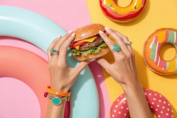 A close up of hands holding a delicious burger with donuts in a colorful arrangement.