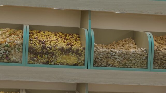 Three adjacent retail bins holding different types of bulk nuts and seeds, including pistachios and possibly almonds or chickpeas. The containers are pastel green and transparent, offering a clean