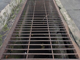 Obraz premium A water channel covered by iron bars that have started to rust is located between the road and the sidewalk