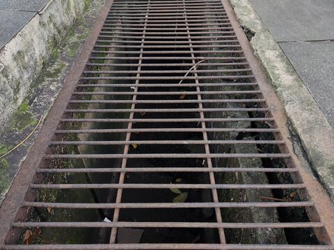 A water channel covered by iron bars that have started to rust is located between the road and the sidewalk - Powered by Adobe
