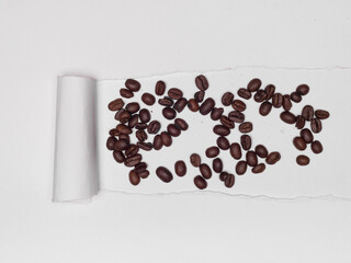 Roasted coffee beans scattered beneath a torn piece of white paper.