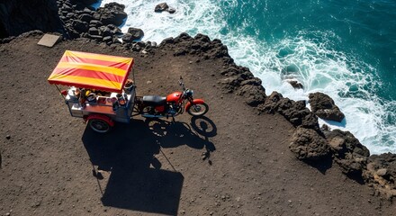 Aerial view of a red motorcycle sidecar parked at the edge of a rocky coastline with turquoise water and a striped canopy