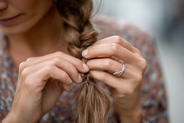 Fototapeta premium Close-up of hands braiding long hair, natural texture and detail, 