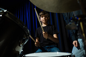 Young caucasian woman teaches a boy to play the drums in the studio on a black background. Music...