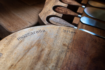 Close-up shot of wooden cheese board with mozzarella and brie engraved, showcasing specific sections for various cheese types, alongside cheese knives