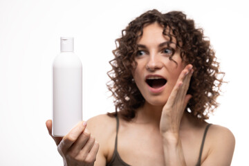 Portrait of an attractive cheerful long-haired curly-haired girl holding a bottle of soap, shampoo,...