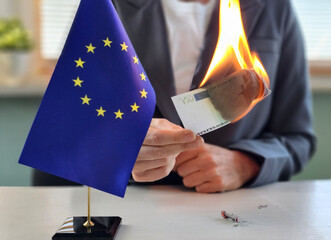 Burns euro note near European Union flag in a provocative act of dissent concept