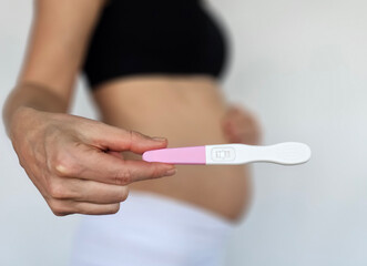 Woman holds pregnancy test in front of her baby bump, celebrating a new beginning