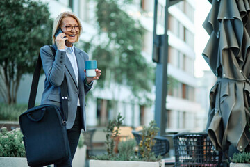 Portrait of a middle aged mature businesswoman woman using a smartphone mobile phone and holding a...