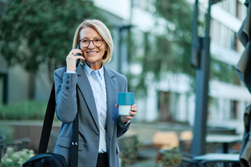 Portrait of a middle aged mature businesswoman woman using a smartphone mobile phone and holding a...