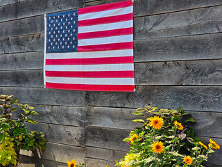 An American flag is displayed on a rustic wooden wall, complemented by vibrant yellow flowers below