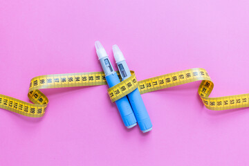 Blue insulin pens and yellow measuring tape on pink background representing weight loss, diabetes treatment, healthcare, and medical control. drugs injection ozempic for weight loss