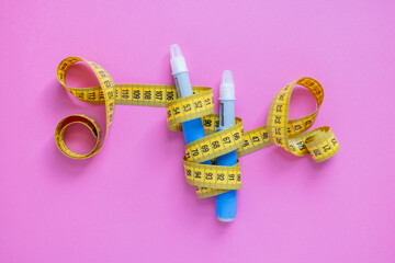 Insulin injection pens and measuring tape on pink surface. Concept of obesity control, diabetes care, and modern medication. drugs injection ozempic for weight loss