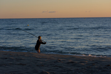 A lone individual stands in the shallow ocean water, silhouetted against a warm sunset sky, holding...